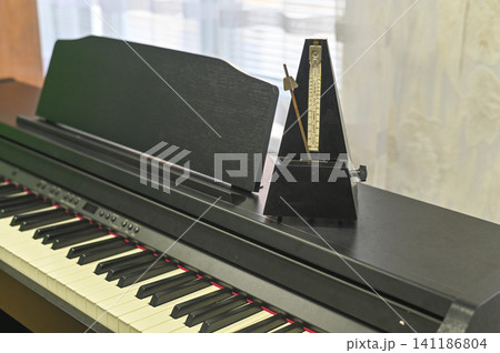 Vintage metronome standing on high-tech electronic piano, emphasizing rhythm and musical discipline Vintage metronome standing on high-tech electronic piano, emphasizing rhythm and musical discipline 141186804