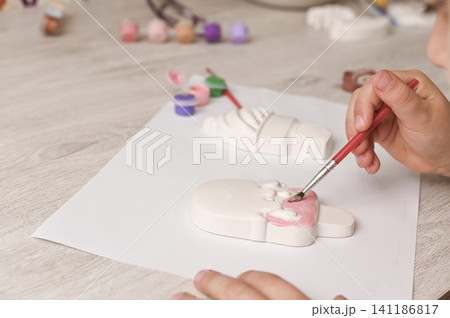 Kid painting white plaster ice cream figurine with small brush. Kid painting white plaster ice cream figurine with small brush. 141186817