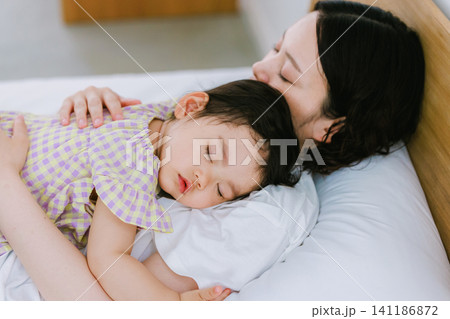 母親とベッドで一緒に寝る女の子   141186872