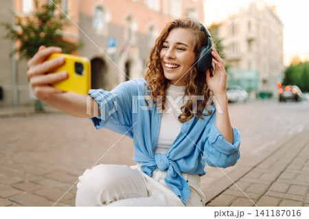 Young woman dancing and listening music with headphones and smart phone in the street. Young woman dancing and listening music with headphones and smart phone in the street. 141187016