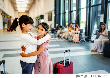 Two girls hugging in airport departures hall with suitcase Two girls hugging in airport departures hall with suitcase 141187057