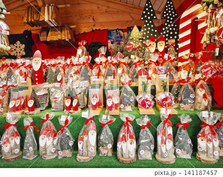Paris, France - December 10, 2025: festive seasonal market stall displays handcrafted wooden Santa figures, Christmas tree ornaments, and Eiffel Tower decorations. Charming holiday souvenir setup 141187457