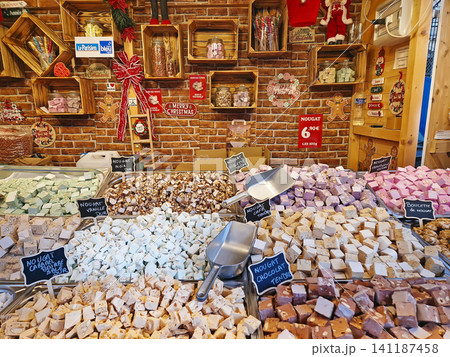 Paris, France - December 10, 2025: Colorful vendor stall displays artisanal nougat cubes in various flavors. Cheerful holiday confectionery atmosphere at the Tuileries Christmas Market 141187458