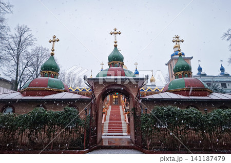 Snowflakes falls gently over an Orthodox monastery, dusting its domes and golden crosses in white snow, while festive lights twinkle in the twilight. Serene winter scene capturing the spiritual beauty Snowflakes falls gently over an Orthodox monastery, dusting its domes and golden crosses in white snow, while festive lights twinkle in the twilight. Serene winter scene capturing the spiritual beauty 141187479