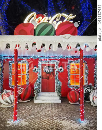 Chisinau, Moldova - January 10, 2026: A festive Coca-Cola themed house brightly decorated for Christmas with giant baubles, snowy eaves, and glowing lights. Magical winter holiday night background 141187483