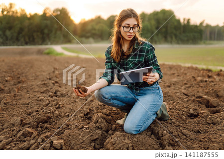 Farmer woman with a digital tablet holds black soil in her hands. Concept of technology, ecology. Farmer woman with a digital tablet holds black soil in her hands. Concept of technology, ecology. 141187555