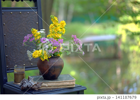 Vintage still life on an old chair with wildflowers and an old book. Vintage still life on an old chair with wildflowers and an old book. 141187679