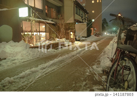 雪が残る夜の犀星の道に佇む自転車と温かな光が漏れる建物 雪が残る夜の犀星の道に佇む自転車と温かな光が漏れる建物 141187803