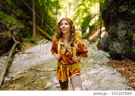 A traveler walks along forest hiking trail in mountains on a sunny day. Outdoor recreation concept. A traveler walks along forest hiking trail in mountains on a sunny day. Outdoor recreation concept. 141187889