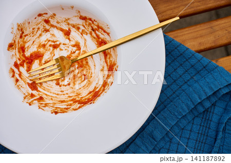 Empty plate with tomato sauce remains and fork on table beside cloth napkin Empty plate with tomato sauce remains and fork on table beside cloth napkin 141187892