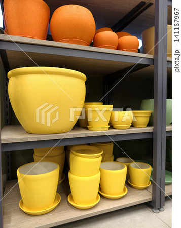 Ceramic flower pots in yellow and red tones with saucers of different sizes displayed in a retail gardening center Ceramic flower pots in yellow and red tones with saucers of different sizes displayed in a retail gardening center 141187967