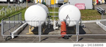 Two industrial metal liquefied gas tanks with pipeline connections at a public gas station and a red fire extinguisher placed close Two industrial metal liquefied gas tanks with pipeline connections at a public gas station and a red fire extinguisher placed close 141188008