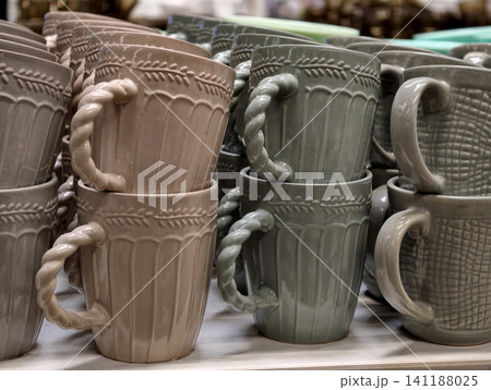Ceramic cups in deep dark shades with twisted handles arranged on store shelves showing basic tableware assortment intended for daily kitchen use and practical retail presentation Ceramic cups in deep dark shades with twisted handles arranged on store shelves showing basic tableware assortment intended for daily kitchen use and practical retail presentation 141188025