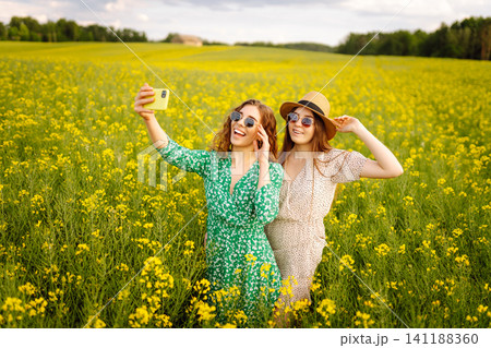 Two Young woman takes a selfie while walking flowering field. Relax and lifestyle. Summer landscape. Two Young woman takes a selfie while walking flowering field. Relax and lifestyle. Summer landscape. 141188360