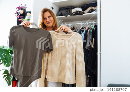 middle-aged woman tries on clothes from her home wardrobe middle-aged woman tries on clothes from her home wardrobe 141188707