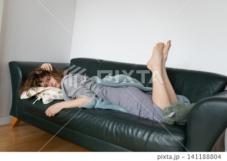 young red-haired woman relaxing on leather sofa 141188804