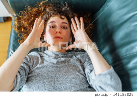 young red-haired woman relaxing on leather sofa 141188829