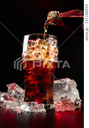 Sparkling cola is poured from a bottle into a misted glass with ice. Sparkling cola is poured from a bottle into a misted glass with ice. 141188950