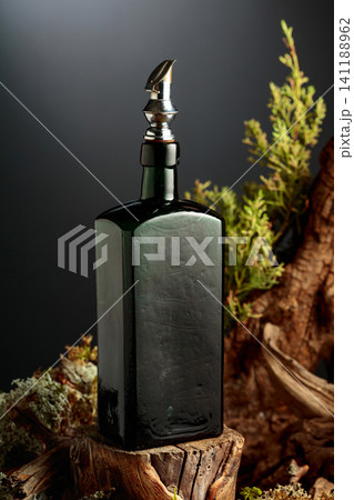 Vintage bottle of gin or herbal bitter, set among juniper branches, weathered driftwood and forest moss. Vintage bottle of gin or herbal bitter, set among juniper branches, weathered driftwood and forest moss. 141188962