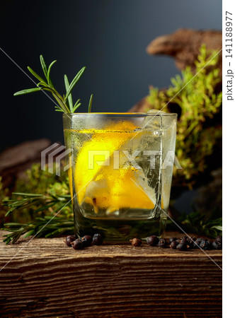 Gin and tonic cocktail with ice, lemon, juniper berries and rosemary sprigs sits on an old weathered board. Gin and tonic cocktail with ice, lemon, juniper berries and rosemary sprigs sits on an old weathered board. 141188977