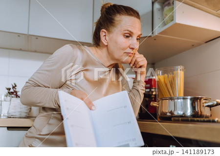 middle-aged woman prepares a recipe for lunch in her home kitchen 141189173