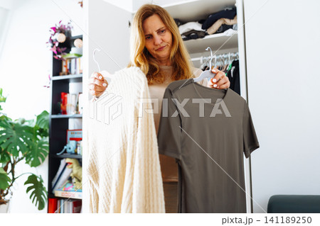 middle-aged woman tries on clothes from her home wardrobe 141189250