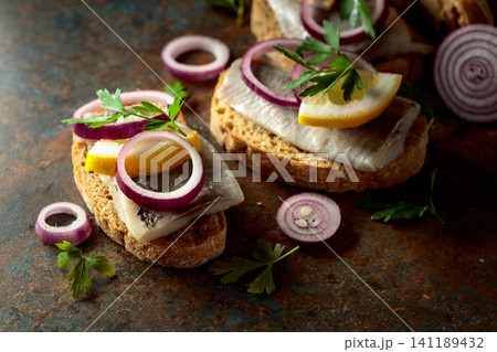 Open sandwiches with herring filet, red onion, lemon, and parsley. Open sandwiches with herring filet, red onion, lemon, and parsley. 141189432