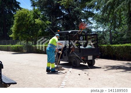 Municipal groundskeeper sweeping park path beside maintenance vehicle in madrid for public works background and environmental upkeep concept 141189503