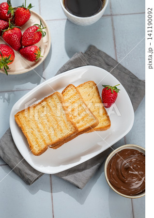 Toasted bread with chocolate cream and strawberry on a plate on a tile background Toasted bread with chocolate cream and strawberry on a plate on a tile background 141190092