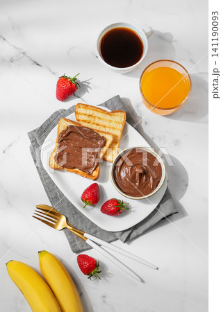Toasted bread with chocolate cream, banana and strawberry on a plate on a marble background Toasted bread with chocolate cream, banana and strawberry on a plate on a marble background 141190093
