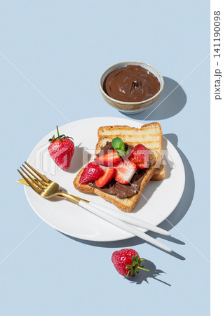 Toasted bread with chocolate cream and strawberry on a white plate on a blue background 141190098