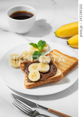 Toasted bread with chocolate cream and banana on a plate on a marble background Toasted bread with chocolate cream and banana on a plate on a marble background 141190102