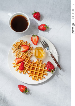 Belgian waffles with fresh strawberries and honey on a white plate on a concrete background 141190112