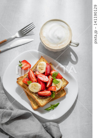 Toasted bread with chocolate cream, strawberries, and banana on a plate on a concrete background 141190129