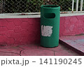 Green cylindrical public trash bin set against a pink hexagonal textured wall 141190245