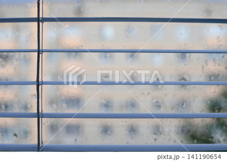 Metal slats of Venetian blinds in a home interior against a raindrop-covered window. Metal slats of Venetian blinds in a home interior against a raindrop-covered window. 141190654
