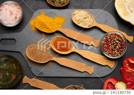 Assorted ground spices in wooden spoons, turmeric, paprika, nutmeg, ginger, dark stone surface 141190736