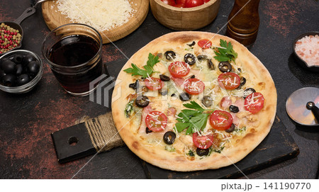 Whole pizza on a wooden board surrounded by tomatoes, olives, herbs, spices and kitchen tools Whole pizza on a wooden board surrounded by tomatoes, olives, herbs, spices and kitchen tools 141190770