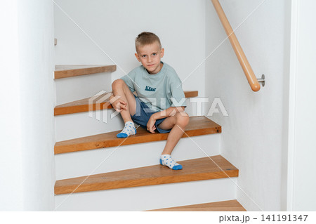 Boy sitting on stairs, in indoor staircase with white walls and wooden handrail, with stairs, wooden handrail, white wall, with wood, plaster texture, from a side view perspective. Boy sitting on stairs, in indoor staircase with white walls and wooden handrail, with stairs, wooden handrail, white wall, with wood, plaster texture, from a side view perspective. 141191347