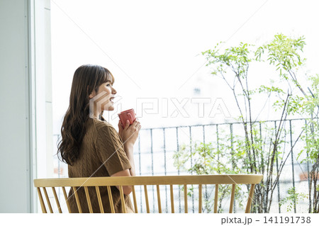 雨の日の窓際でコーヒーを飲む若い女性 141191738
