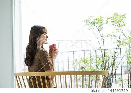 雨の日の窓際でコーヒーを飲む若い女性 141191739