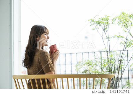 雨の日の窓際でコーヒーを飲む若い女性 雨の日の窓際でコーヒーを飲む若い女性 141191741