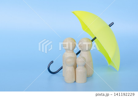 Wooden figures with a yellow umbrella representing security and insurance with customizable space for text. Wooden figures with a yellow umbrella representing security and insurance with customizable space for text. 141192229