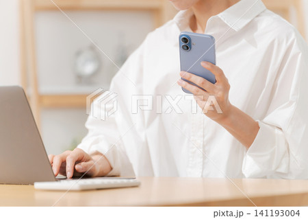 スマホを見ながらパソコンを使う女性 スマホを見ながらパソコンを使う女性 141193004