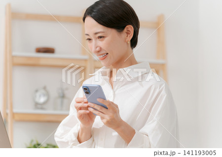 スマホを見ながらパソコンを使う女性 スマホを見ながらパソコンを使う女性 141193005