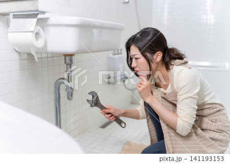 洗面台の水漏れを自分で修理しようとする若い女性 洗面台の水漏れを自分で修理しようとする若い女性 141193153