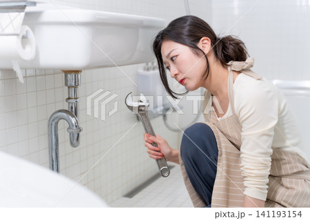 洗面台の水漏れを自分で修理しようとする若い女性 洗面台の水漏れを自分で修理しようとする若い女性 141193154