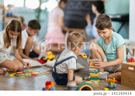 Boy playing in living room of kindergarten, group of children in background Boy playing in living room of kindergarten, group of children in background 141193414