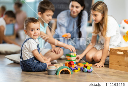 Children of different ages playing with wooden blocks with teacher Children of different ages playing with wooden blocks with teacher 141193436