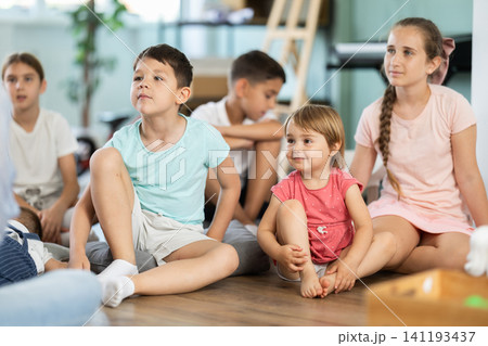 Group of children is sitting on floor, listening to teacher in kindergarten Group of children is sitting on floor, listening to teacher in kindergarten 141193437